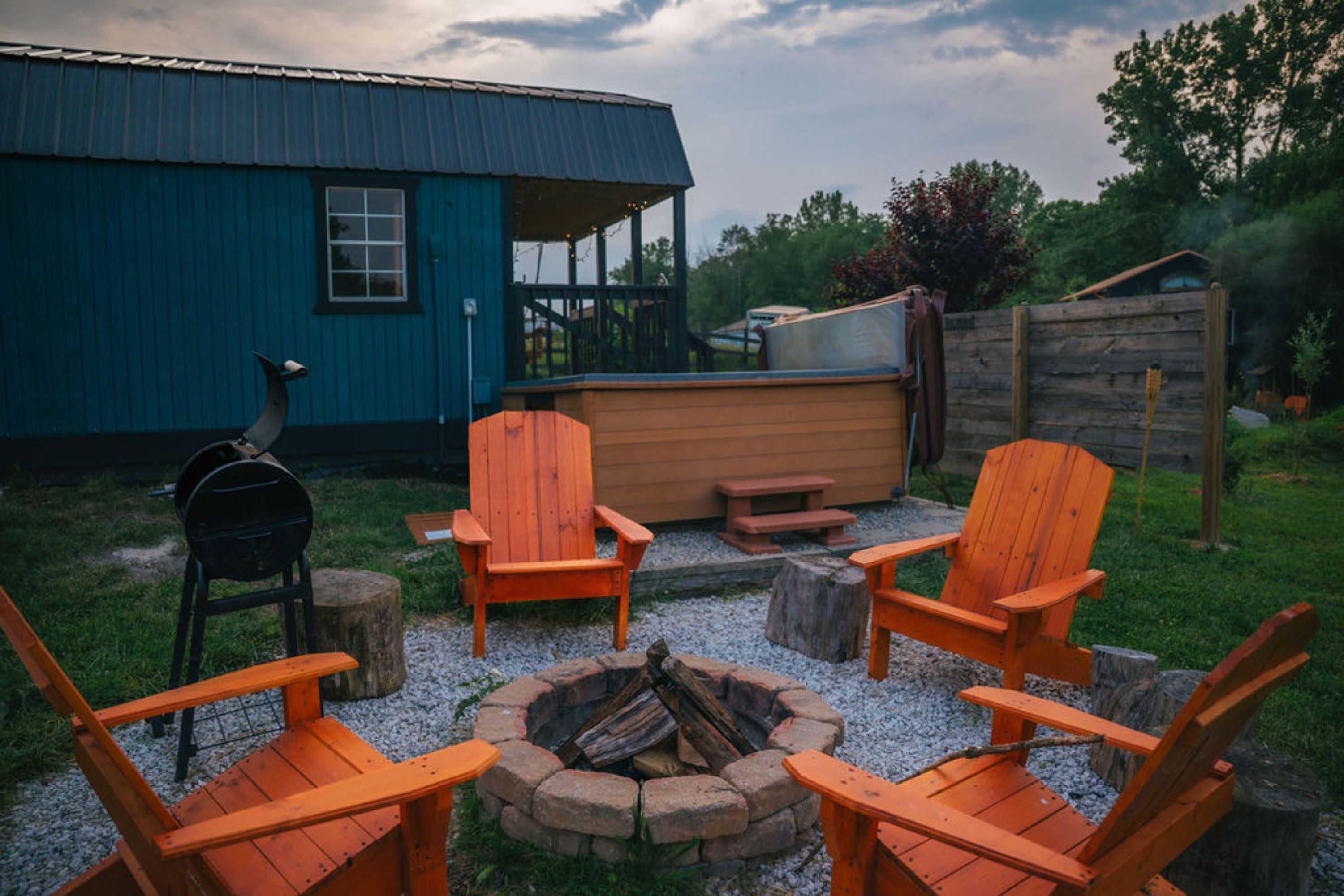 Ein rustikaler Außenbereich mit Holz-Adirondack-Stühlen und einem Feuerkorb, umgeben von einem Kiesweg und einer Holzterrasse.
