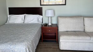 Une chambre d’hôtel avec un lit, une table de chevet avec une lampe, un canapé et un tableau encadré au mur.