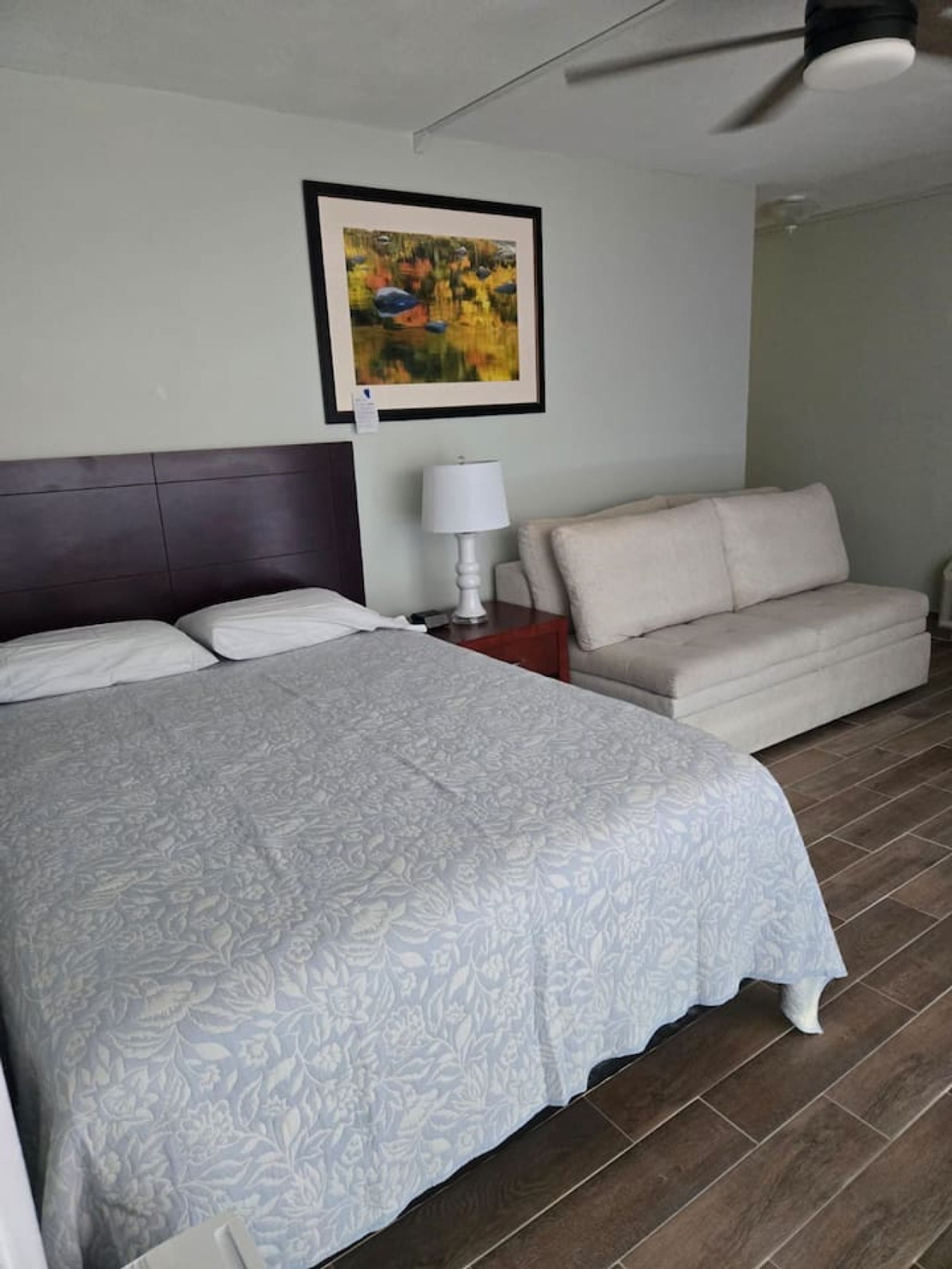 A hotel room with a large bed, a sofa, a nightstand with a lamp, and a ceiling fan.