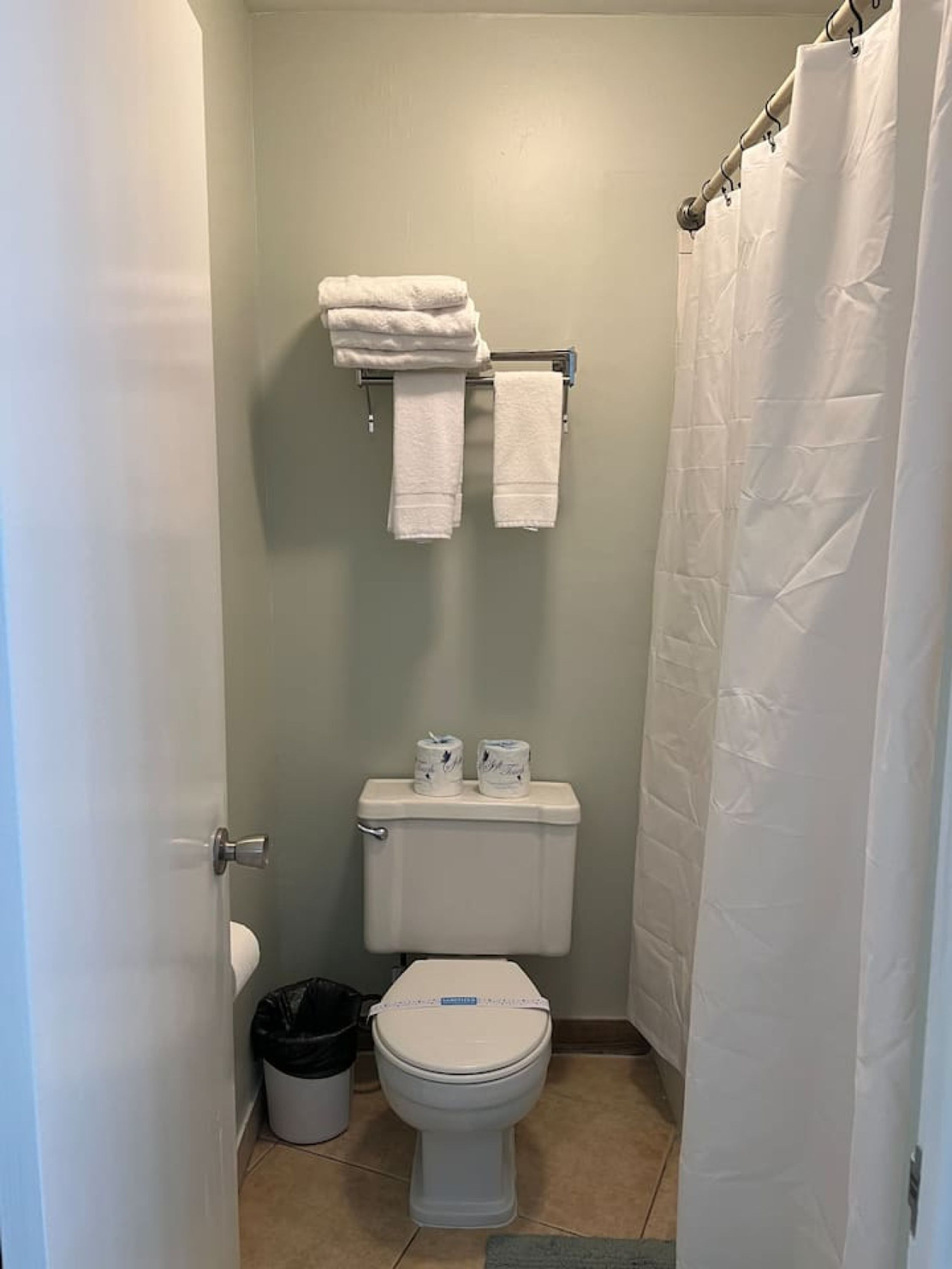 A small bathroom with a toilet, two rolls of toilet paper, a trash can, and a towel rack with two towels.