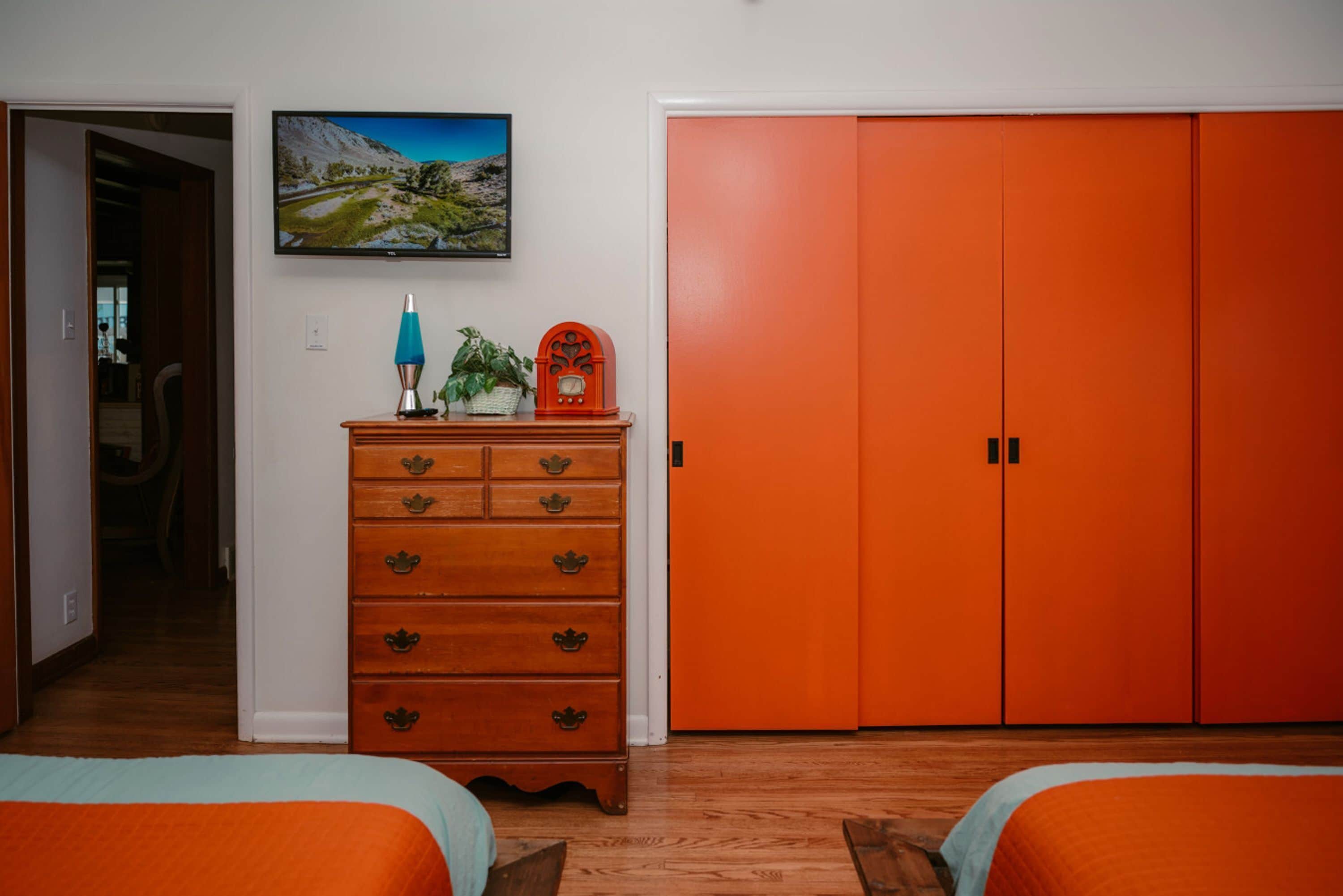 Un dormitorio con dos camas, un armario naranja, un aparador de madera, un televisor y un cuadro en la pared.