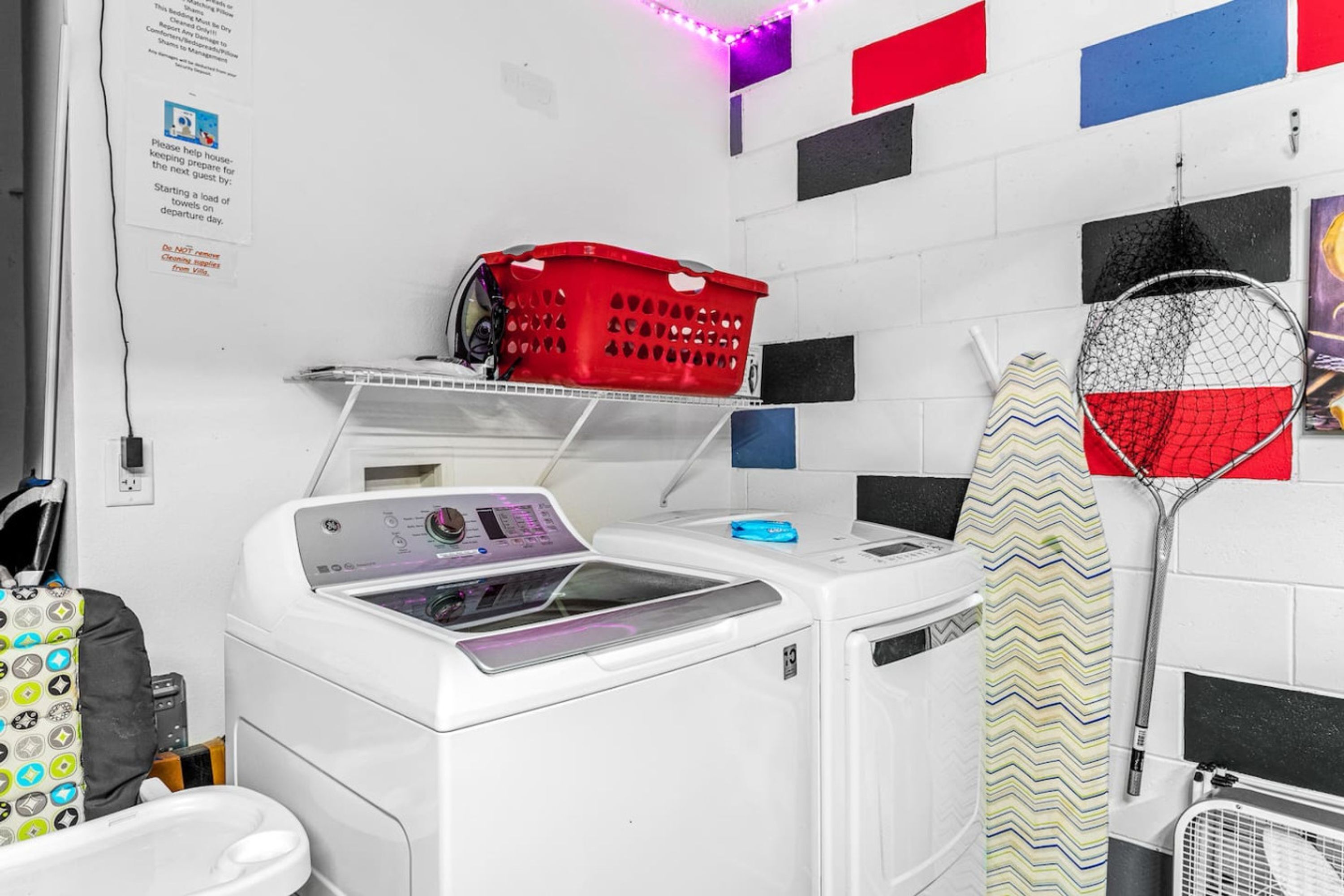 A laundry area with a washing machine, a drying rack, and a red basket on a shelf.