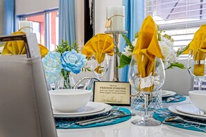 A table set with white plates, blue napkins, and clear glassware, with a framed quote card and floral arrangements. - 4Br Funoasis Pool BBQ Solana (Davenport)