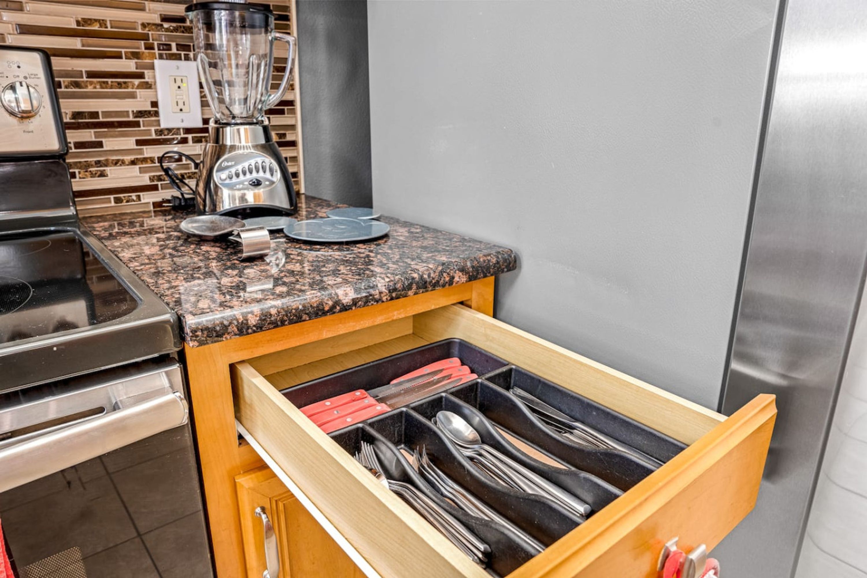 Una cocina con encimera de granito, una licuadora y un organizador de cajones con utensilios.