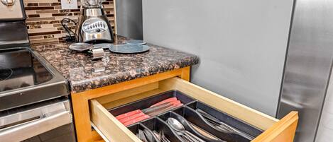 Una cocina con encimera de granito, una licuadora y un organizador de cajones con utensilios.