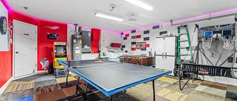 Una habitación con mesa de ping pong, mesa de fútbol de mesa y aro de baloncesto.