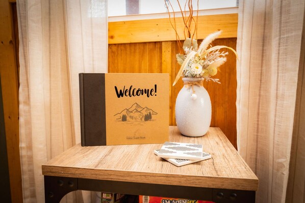 A wooden table with a welcome sign, a guest book, and a vase with dried flowers. - Ruby s Red Cabin Hot Tub Nature Horses Indy (Indianapolis)