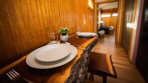 Un interior de madera con una mesa de comedor preparada para dos personas, una silla y una planta pequeña.