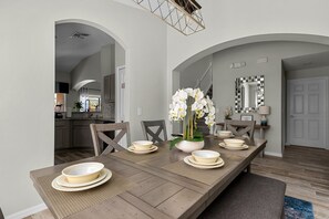 Comedor con una larga mesa de madera dispuesta para cuatro personas, rodeada de sillas. Hay un jarrón con flores blancas sobre la mesa.