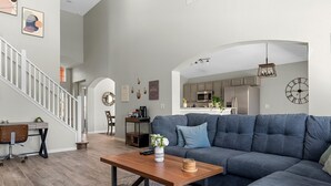 A spacious living room with a grey sectional sofa, a wooden coffee table, and a staircase leading to an upper level.