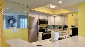 Eine moderne Küche mit Edelstahl-Kühlschrank, Mikrowelle und Backofen. Es gibt eine Marmorarbeitsplatte und ein Spülbecken mit Armatur. Die Küche verfügt über weiße Schränke und eine gelbe Akzentwand.
