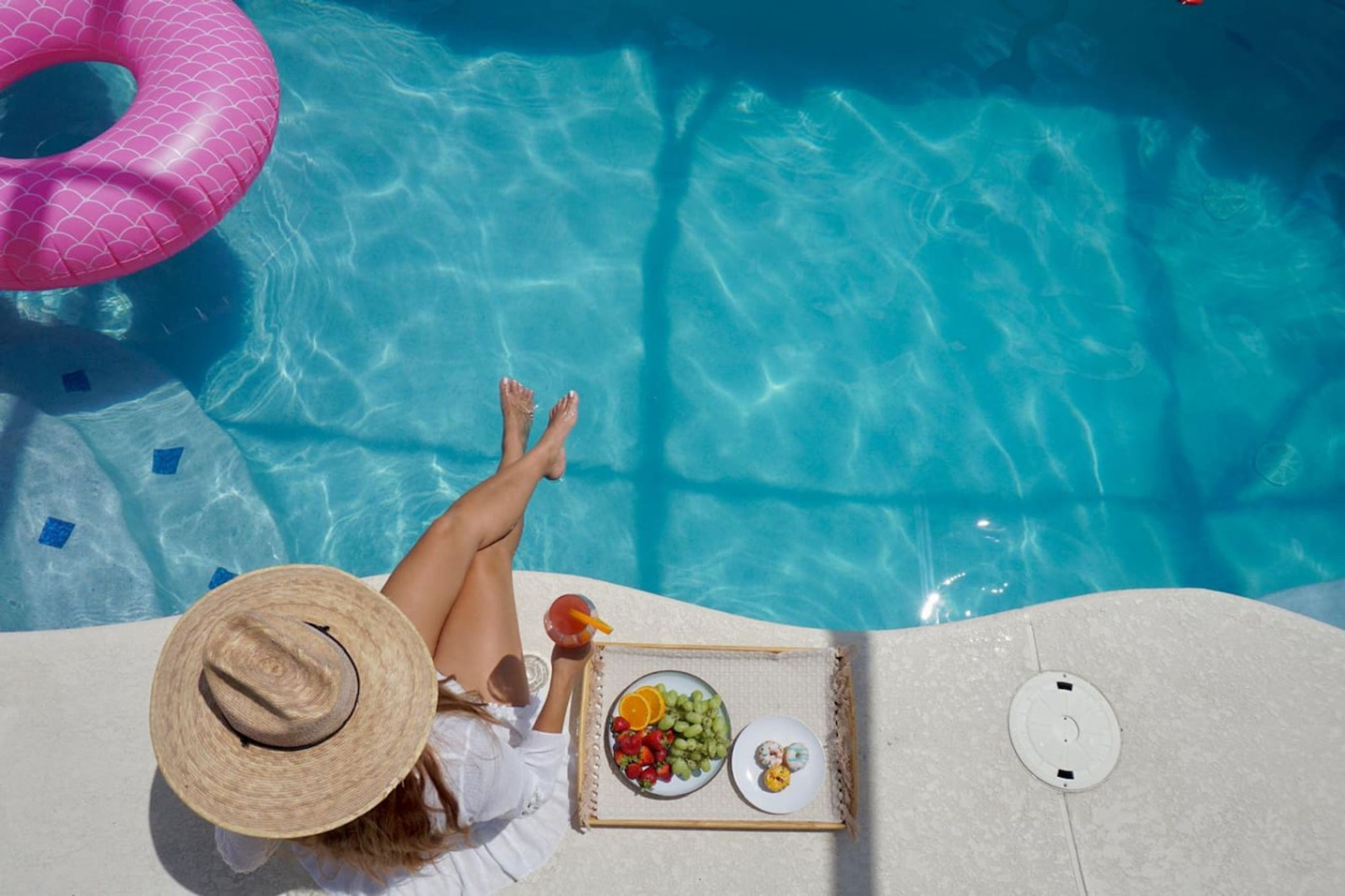 Une vue sur la piscine avec une personne se relaxant, un flotteur rose et un plateau avec de la nourriture et des boissons.