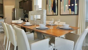 A modern kitchen with a wooden dining table set for six, white chairs, and a marble island.