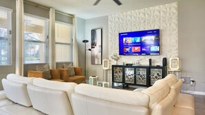 A living room with a white leather sofa, a television mounted on the wall, and a decorative cabinet.
