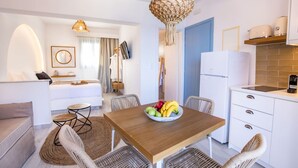 A modern kitchen with a wooden table, wicker chairs, and a fruit bowl. - Yploui Suites 3 (Karpathos)