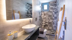 A modern bathroom with a large mirror, a vessel sink, and a shower with patterned tiles. - Yploui Suites 3 (Karpathos)