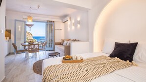 A modern bedroom with a large bed, a dining area, and a view of the sea. - Yploui Suites 3 (Karpathos)