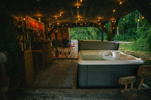 Een hottub onder een houten pergola met lichtjes, omringd door groen.