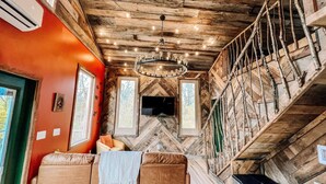 Interior acogedor de una cabaña con techo de madera, un sofá y una escalera.