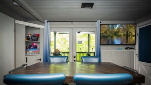 A dining area with a wooden table and blue chairs, a shelf with toiletries, and a view of a river through a glass door. - Lakefront-nestled in Nirvana (Martinsville)