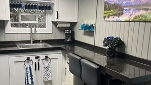 A modern kitchen with white cabinets, a stainless steel sink, a coffee maker, and a bar area with stools. - Lakefront-nestled in Nirvana (Martinsville)