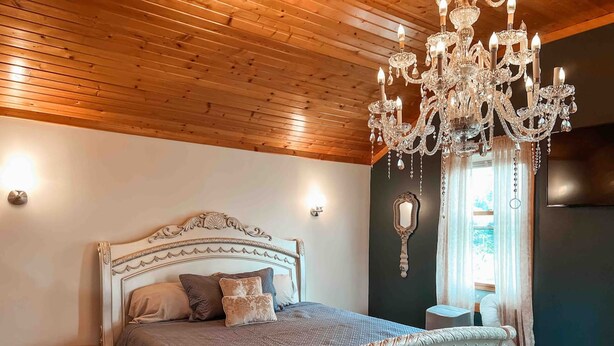 A bedroom with a wooden ceiling, a white ornate bed, a chandelier, and a mirror on the wall.