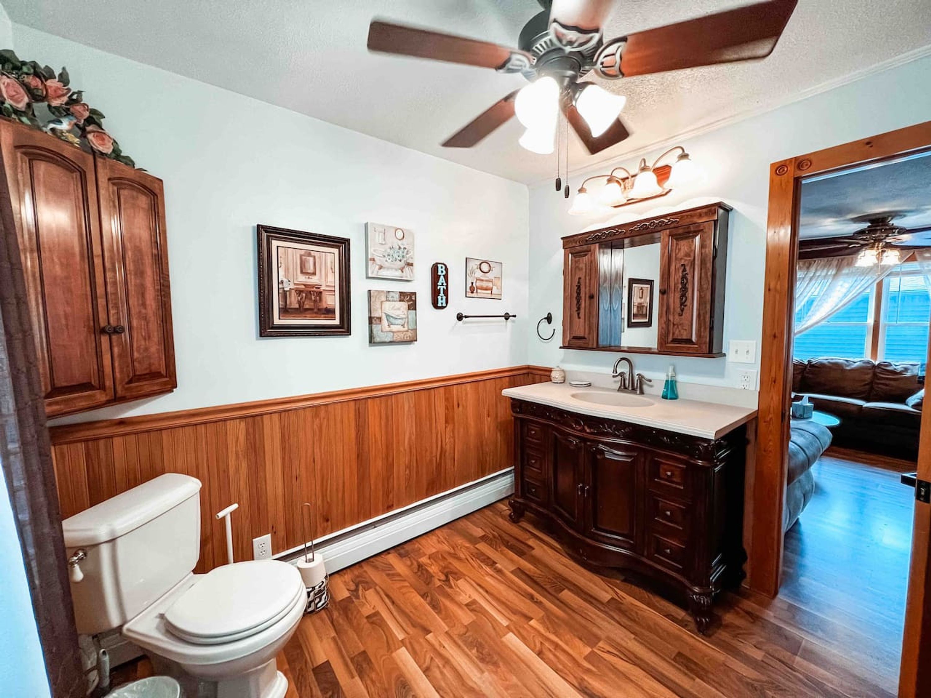 Un baño con muebles de madera, un inodoro, un tocador con espejo y cuadros en la pared.