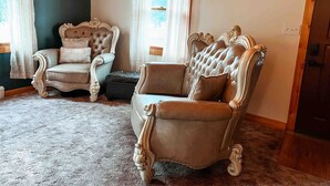 A room with two ornate armchairs, a small table, and a window with curtains.