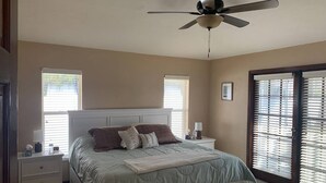 Ein Schlafzimmer mit Bett, Nachttischen, Deckenventilator und Fenster mit Jalousien.