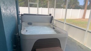 Ein Whirlpool mit integriertem Sitz und Treppen für den Zugang, umgeben von einer überdachten Terrasse mit Blick auf einen weißen Zaun und Grünpflanzen.