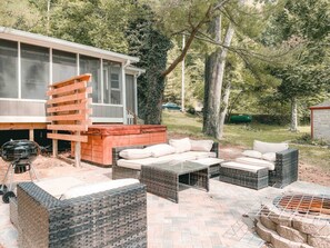 An outdoor patio area with wicker furniture, a grill, and a stone fire pit. - Two Lakefront Cabins Next Door (Martinsville)
