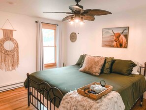 A bedroom with a bed, a ceiling fan, a window, and a wall-mounted macrame wall hanging. - Two Lakefront Cabins Next Door (Martinsville)