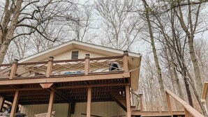 A wooden cabin with a balcony, a stone wall, and a staircase leading up to it. - Two Lakefront Cabins Next Door (Martinsville)