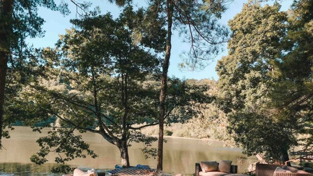 An outdoor seating area with wicker furniture and a hot tub, surrounded by trees and a lake. - Two Lakefront Cabins Next Door (Martinsville)