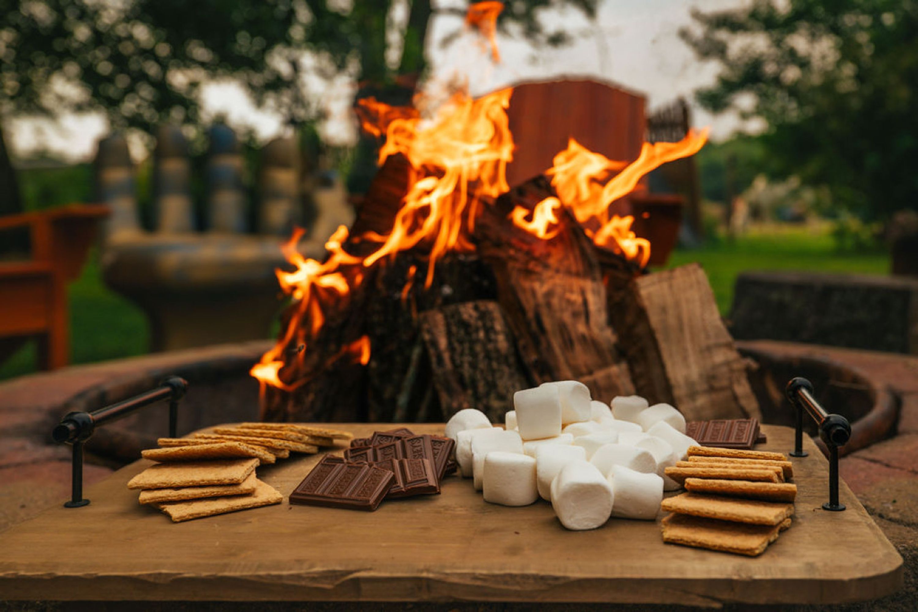 Una fogata con malvaviscos, chocolate y galletas graham sobre una tabla de madera.
