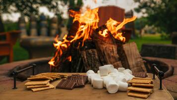 Una fogata con malvaviscos, chocolate y galletas graham sobre una tabla de madera.