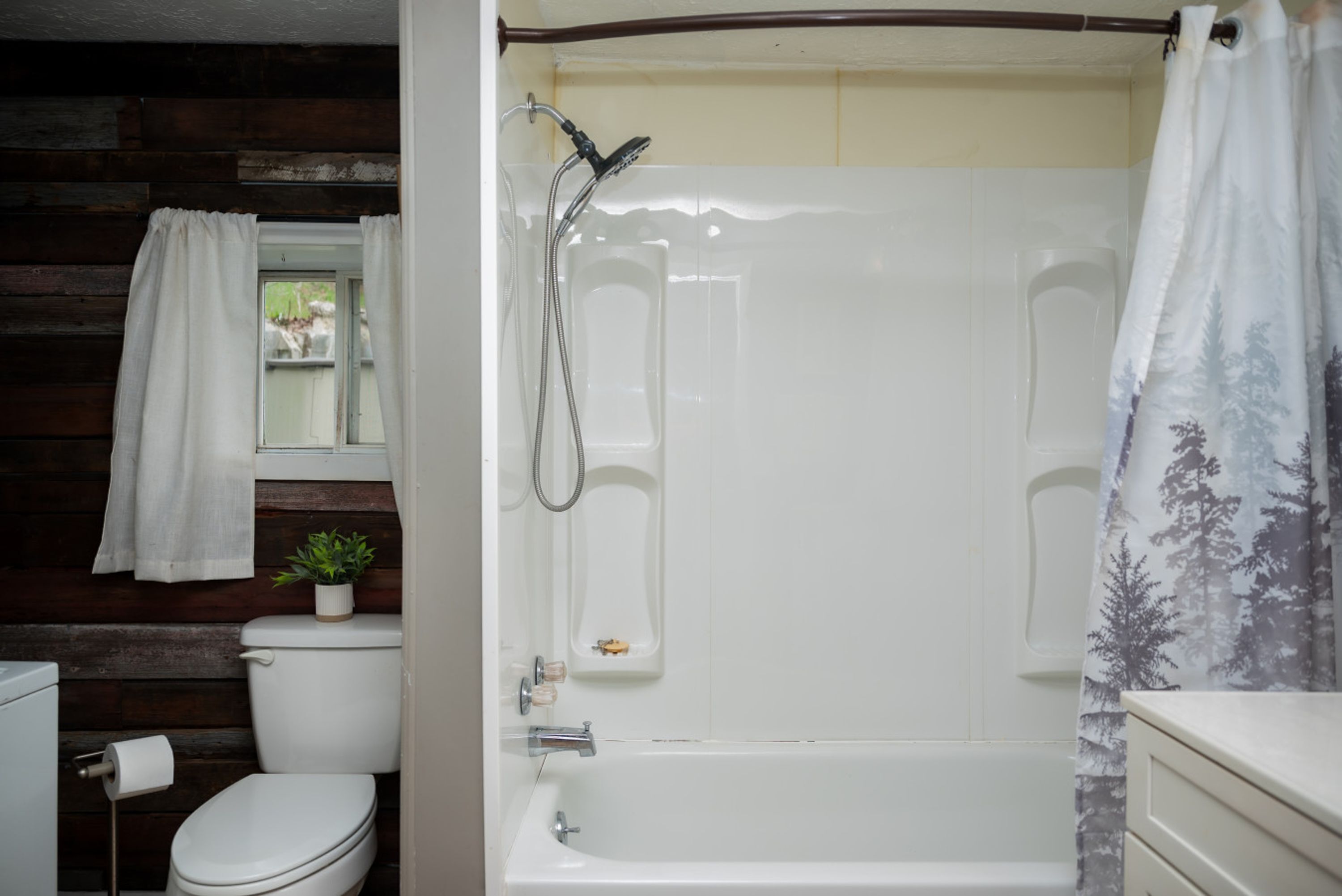 A bathroom with a toilet, a shower with a curtain, and a small potted plant.