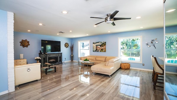 A spacious living room with a flat-screen TV, a sofa, a coffee table, and a ceiling fan. - Fun Pool Relax16miles Bushgarden (Tampa)
