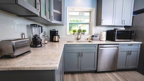 A modern kitchen with grey cabinets, a built-in dishwasher, a toaster, a coffee maker, and a microwave. - Fun Pool Relax16miles Bushgarden (Tampa)