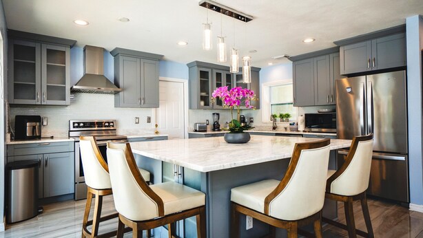 A modern kitchen with grey cabinets, stainless steel appliances, and a marble island with bar stools. - Fun Pool Relax16miles Bushgarden (Tampa)