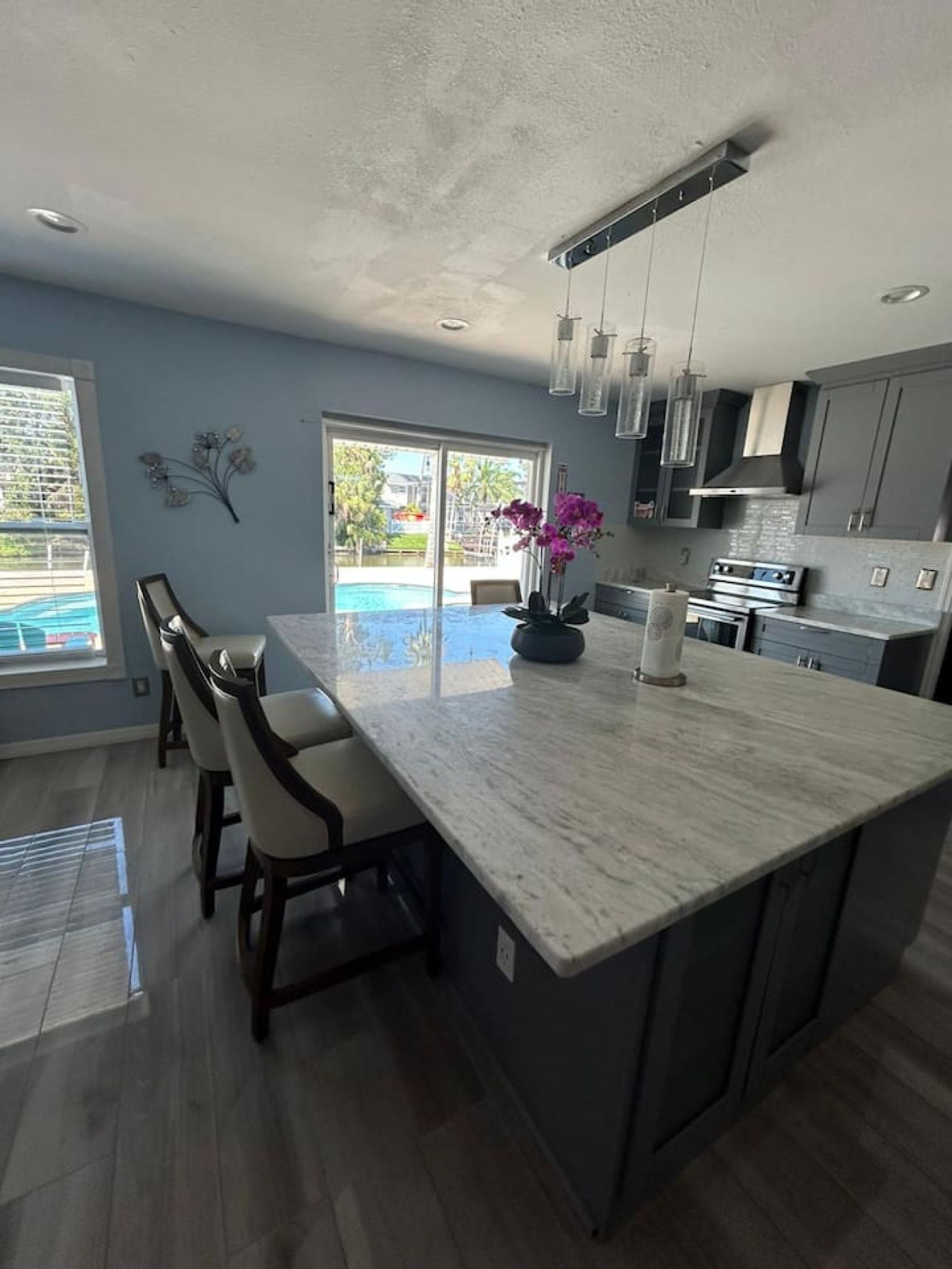 A modern kitchen with a large island, bar stools, and a view of a swimming pool.