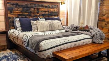 Un dormitorio acogedor con cabecera de madera, cama con ropa de cama estampada, un banco y una alfombra azul y beige.