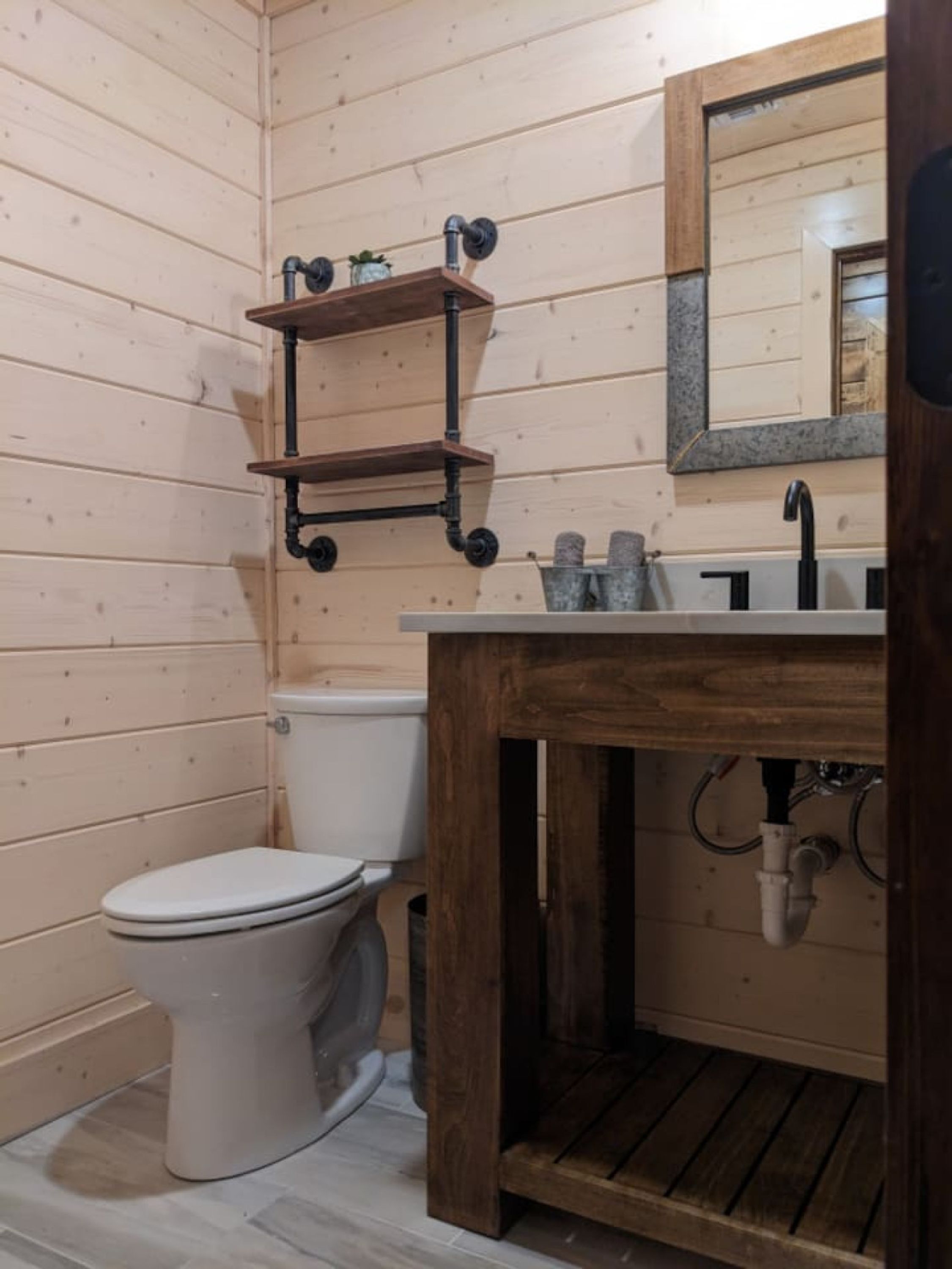 A wooden bathroom with a toilet, a sink, and a mirror.