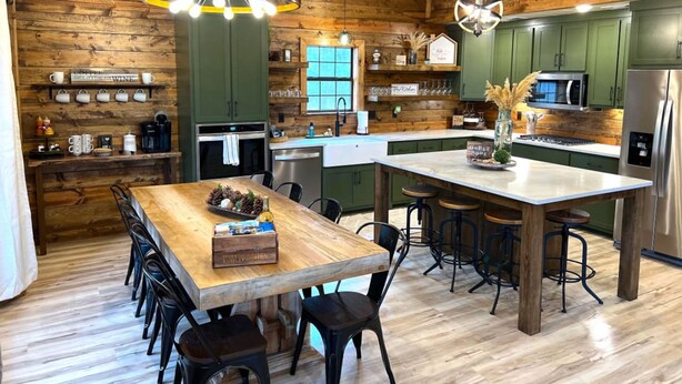 A modern kitchen with wooden walls, green cabinets, and a central island with bar stools. - Lofted Pines Hot Tub Arcade Air Hockey (Broken Bow)