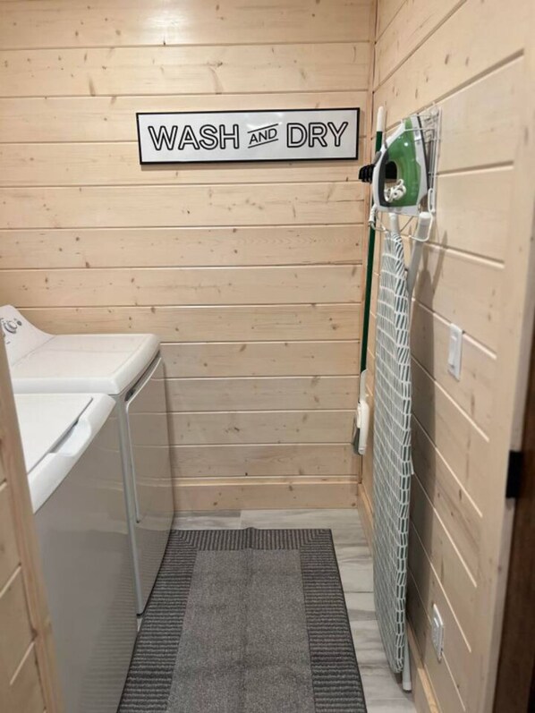 Pequeño cuarto de lavado y secado con pared de madera, lavadora y tendedero.