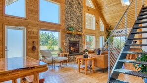 A spacious living room with a stone fireplace, wooden floors, and a staircase.