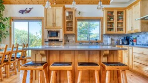 A spacious kitchen with wooden cabinets, a central island with bar stools, a microwave, and a large window providing a view of the outdoors.