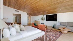 A modern living room with a wooden ceiling, a white sofa, a grey couch, and a brown rug.