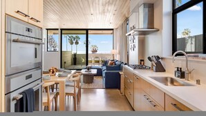 A modern kitchen with a dining area, large windows, and a view of the beach.