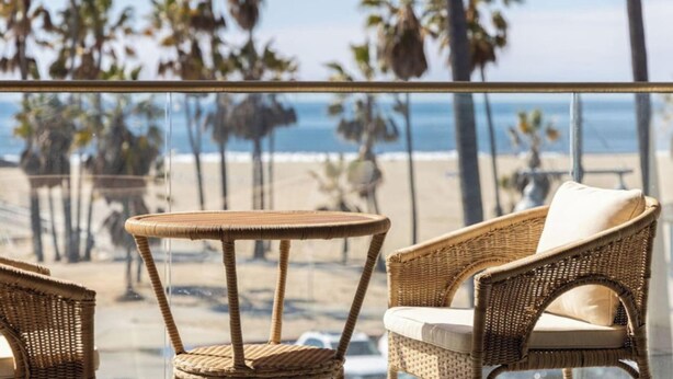 A balcony with wicker furniture overlooking a beach with palm trees and the ocean.